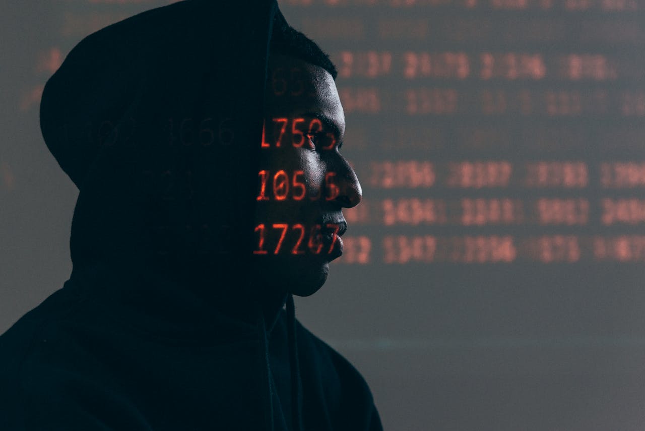 About Side profile of a man in a hoodie, surrounded by red code, depicting cybersecurity theme.